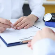 Manos de doctor revisando un expediente médico o formulario con paciente en la primera consulta en León Gto.