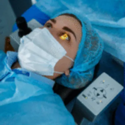 A close up of a female patient wearing a surgical mask and cap, looking up with bright lights in her eyes, preparing for her eye surgery in Mexico at a modern clinic.